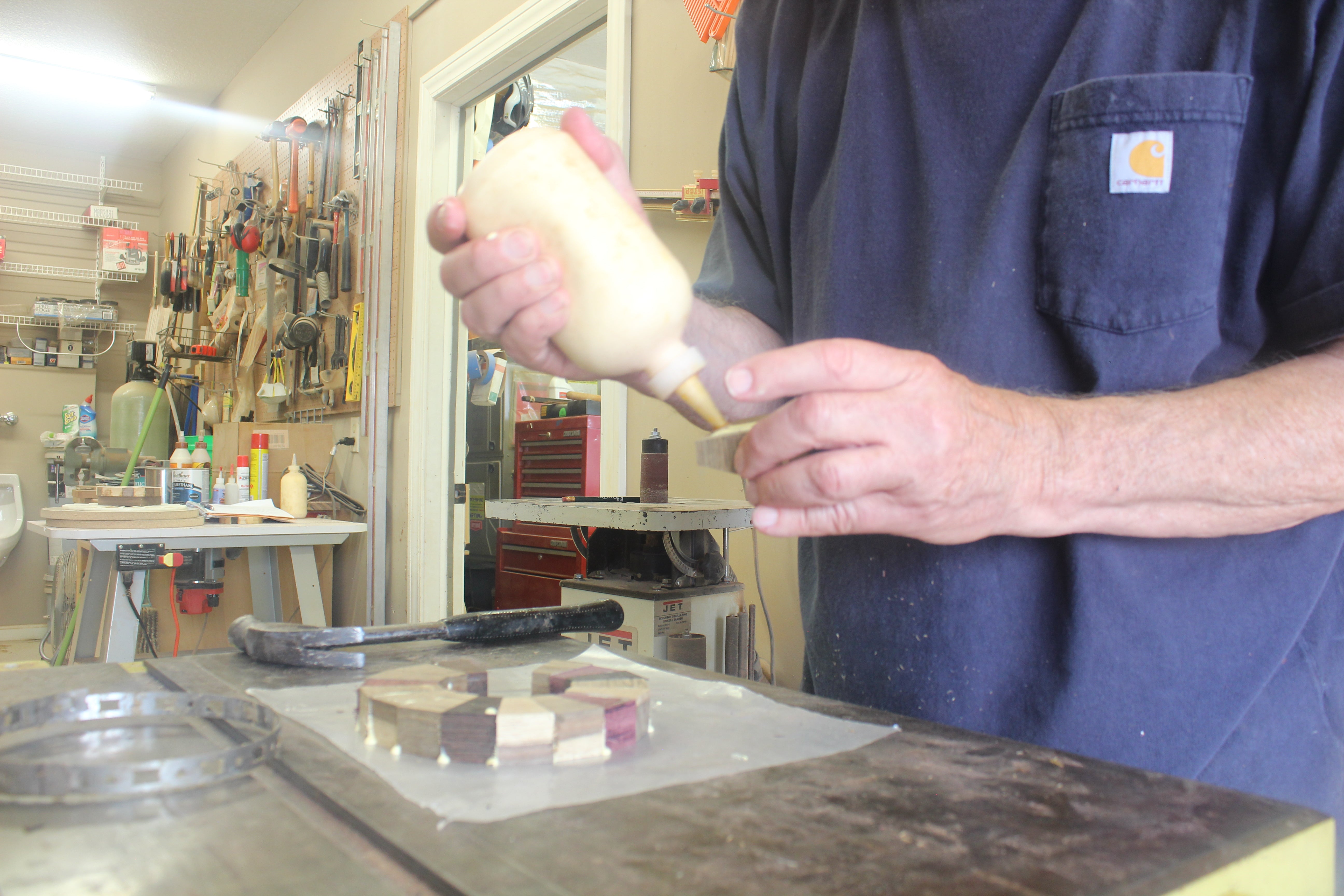 Person holding a tool in a workshop setting while gluing together uniquely made wood working pieces