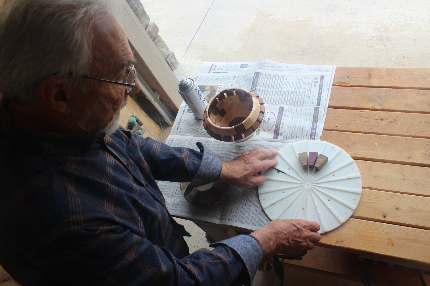 Man working on a craft project at a wooden table with newspapers underneath.
