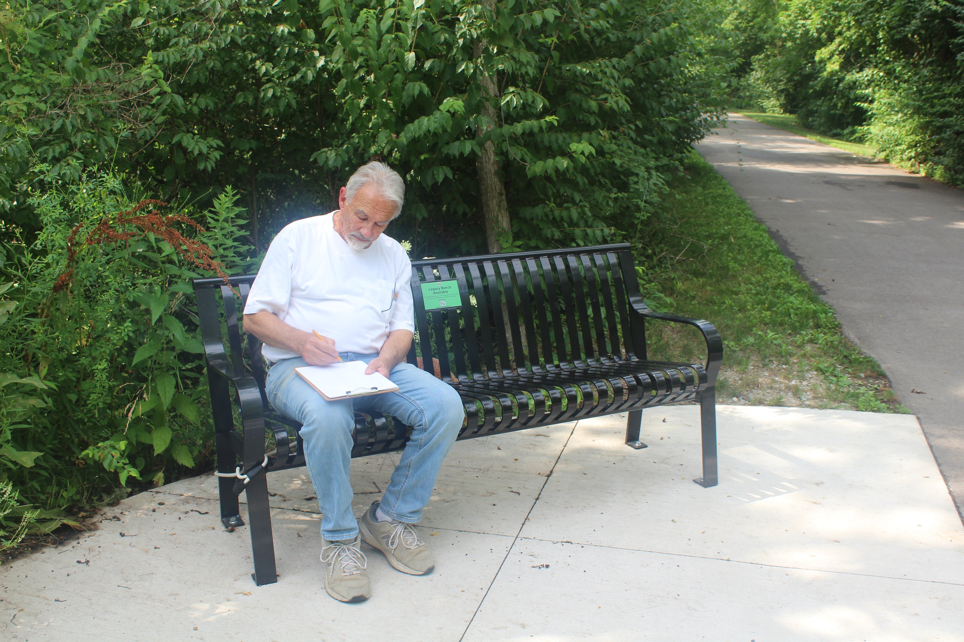 Man sitting on a park bench reading a book with greenery in the background