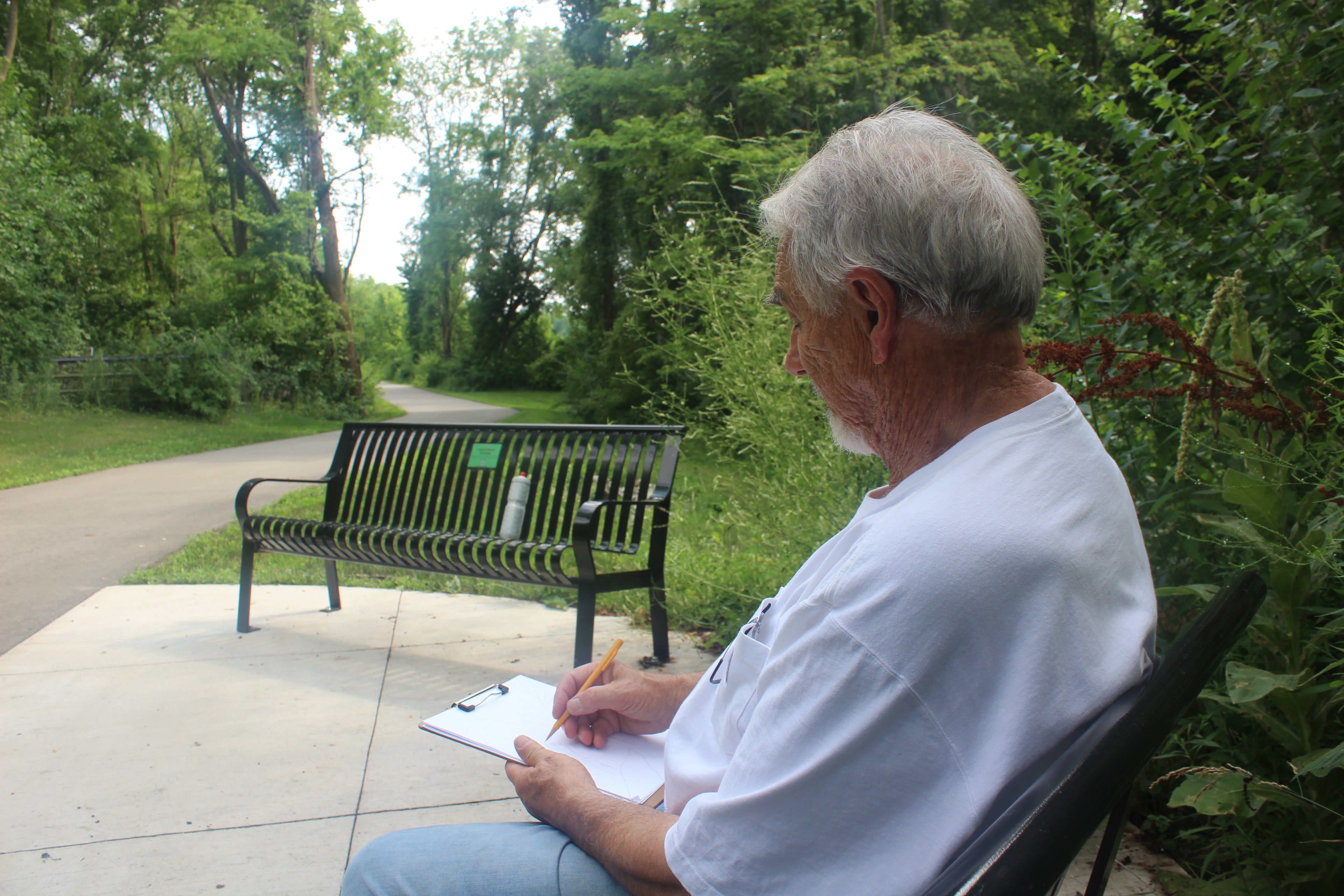 Man sitting while look at trees in order to draw a design for the project he is working on. Thom Pabst Creations.