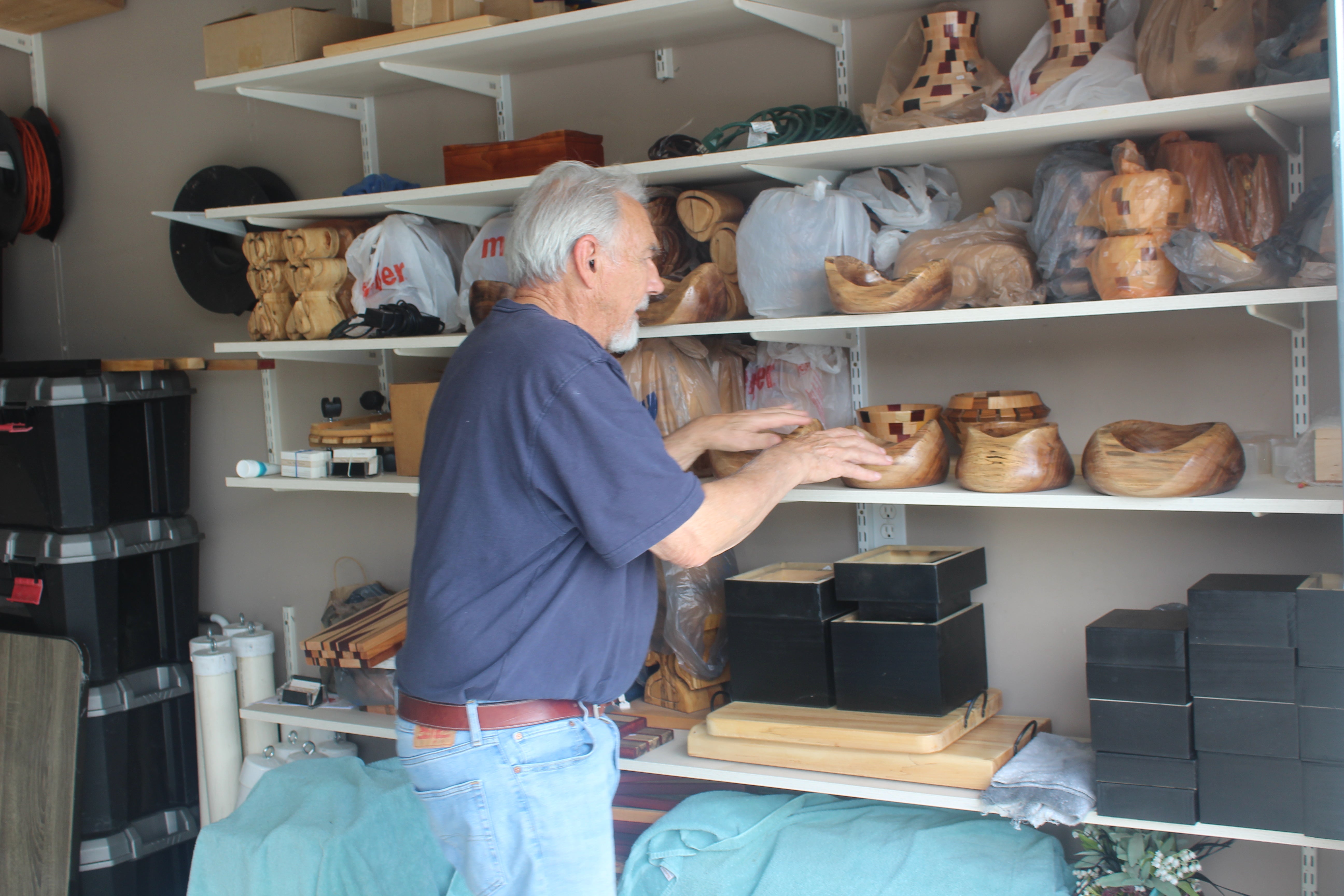 Man browsing wooden items on shelves in a storage or display area.