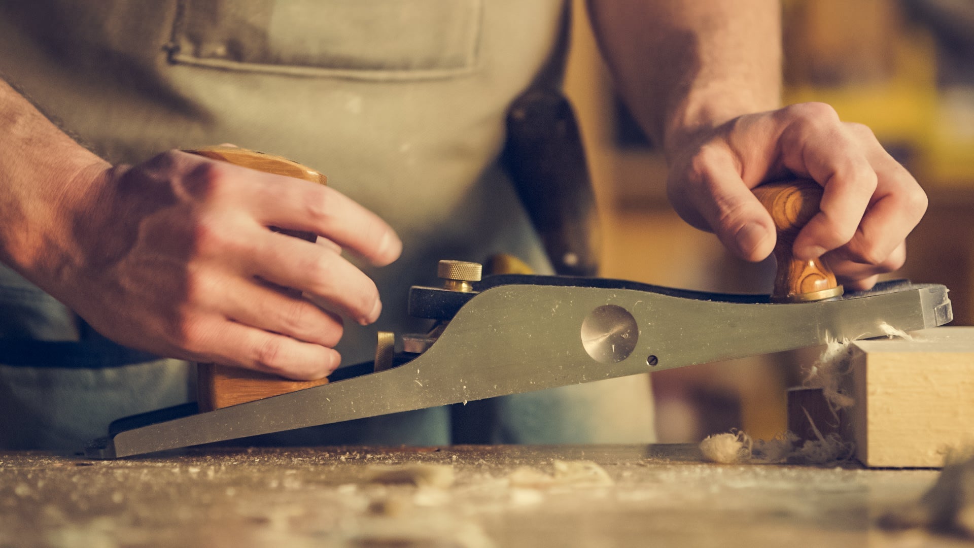 Person using a hand plane on a wooden surface making unique hand-made wood crafting pieces